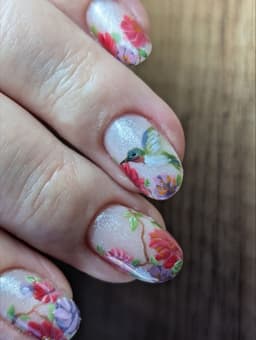 Shimmer base nails with hand-painted floral designs and a detailed hummingbird – a bespoke artistic manicure at MissbehaveNails in Leighton Buzzard.